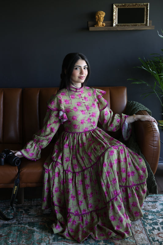 Person wearing a green dress with pink floral pattern sitting on a brown chair.