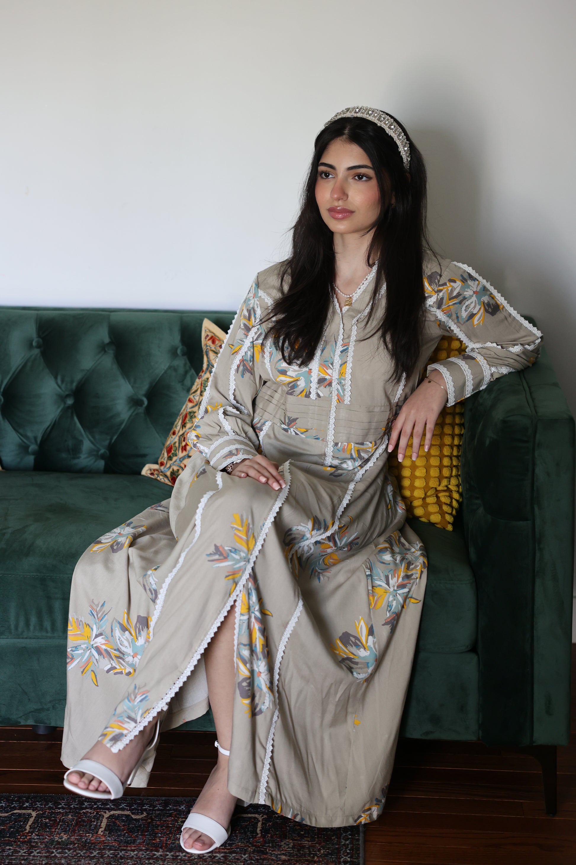 Woman in a embroidered maxi dress sitting on a green couch.